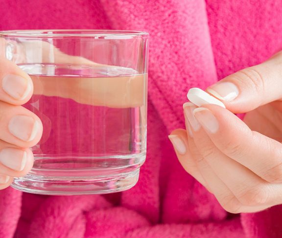 Kvinde holder tøvende et glas vand og en pille
