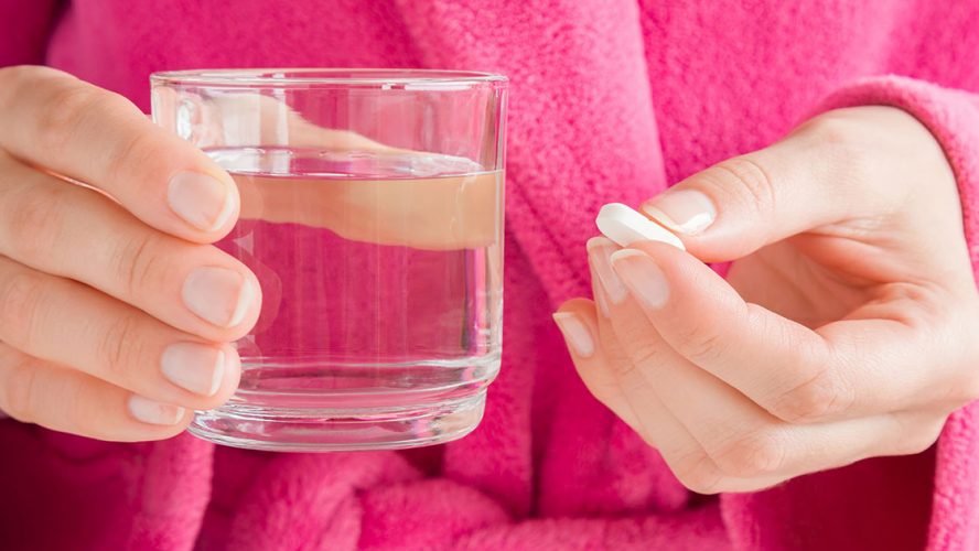 Kvinde holder tøvende et glas vand og en pille