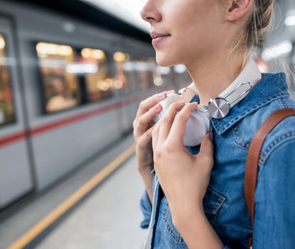 Unrecognizable young woman in denim shirt with earphones, standing at the underground platform, waiting to enter a train