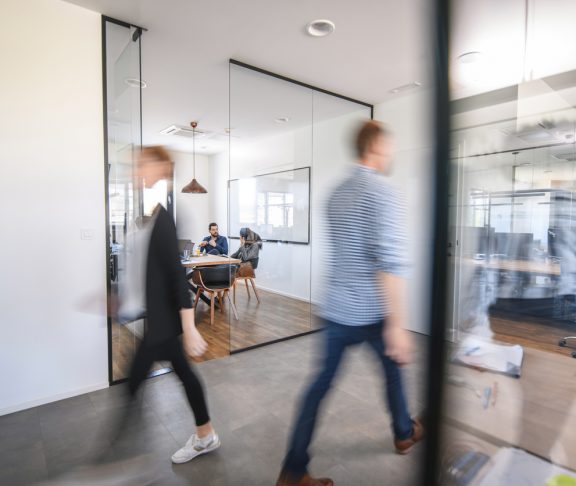 Blurred motion of male and female businesspeople walking down hallway contrasted by still and careful debate of new ideas in the conference room.