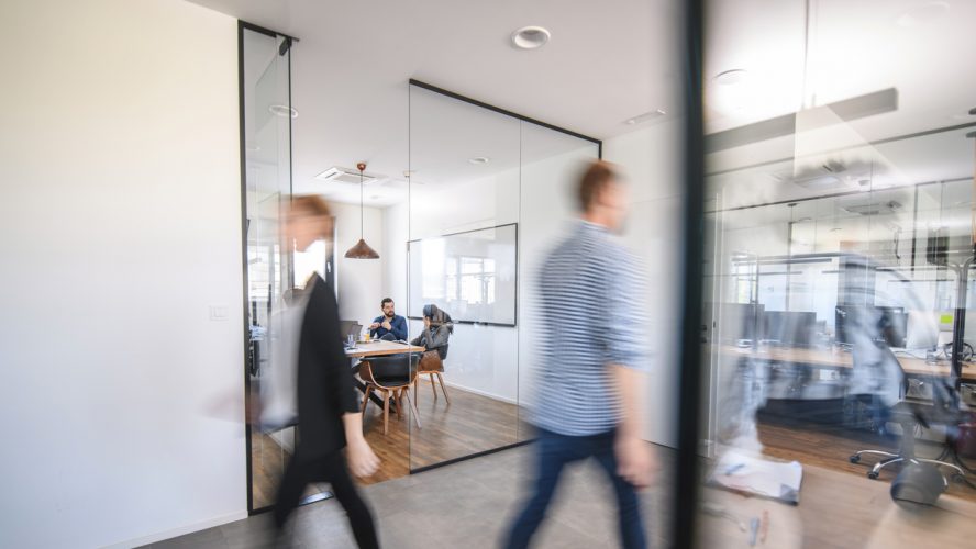 Blurred motion of male and female businesspeople walking down hallway contrasted by still and careful debate of new ideas in the conference room.