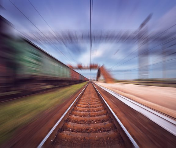 Railway station with cargo wagons in motion at sunset. Railroad with motion blur effect. Railway platform at dusk. Heavy industry. Conceptual background