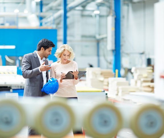 Young businessman reporting production details to senior female manager at factory shopfloor