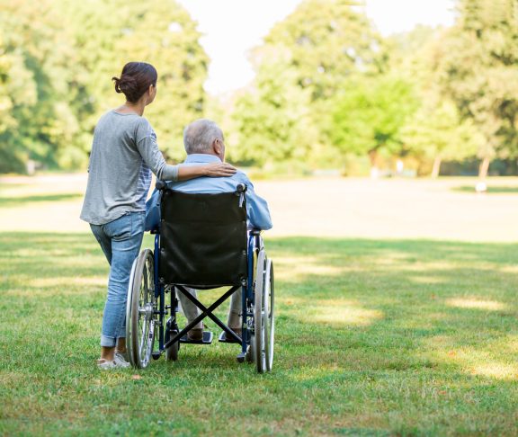 Caregiver and senior man on a wheelchair walking outdoors in a park