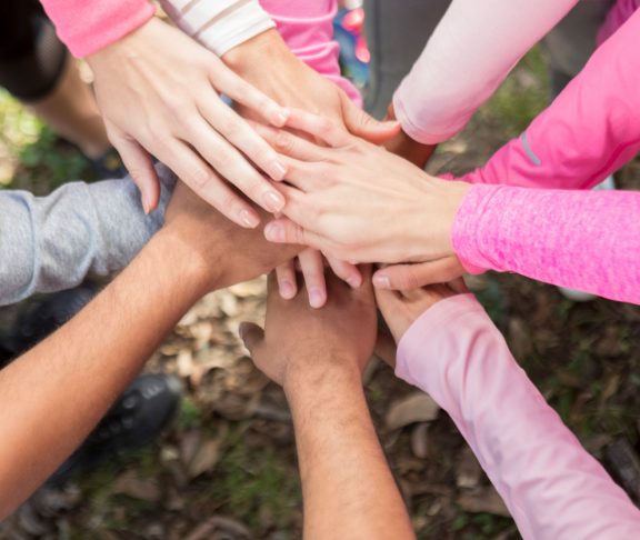 Diverse group of unrecognizable people have their hands together in unity during breast cancer awareness event