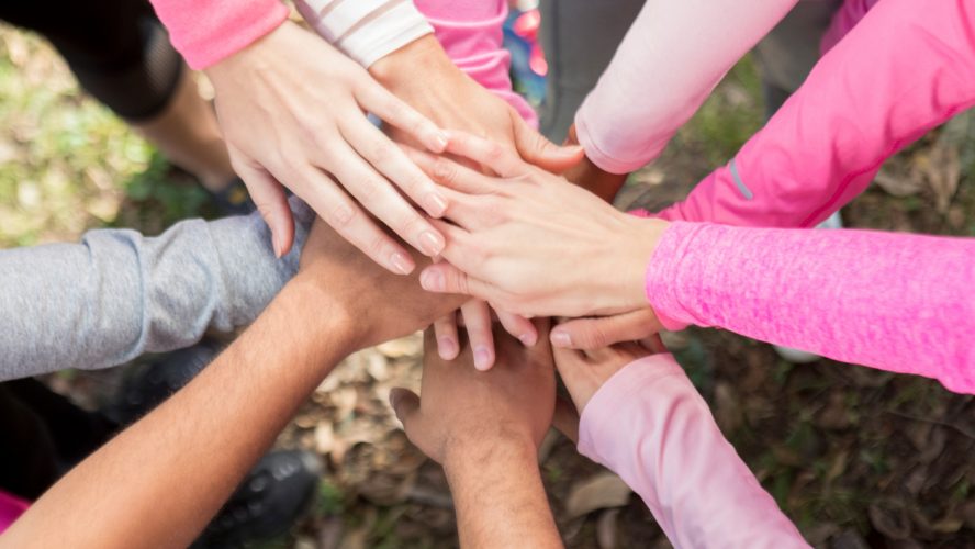 Diverse group of unrecognizable people have their hands together in unity during breast cancer awareness event