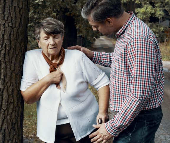 Helpful pedestrian taking care of senior woman having heart attack on the street