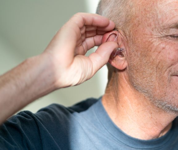 Senior male puts in hearing aid at the start of the day