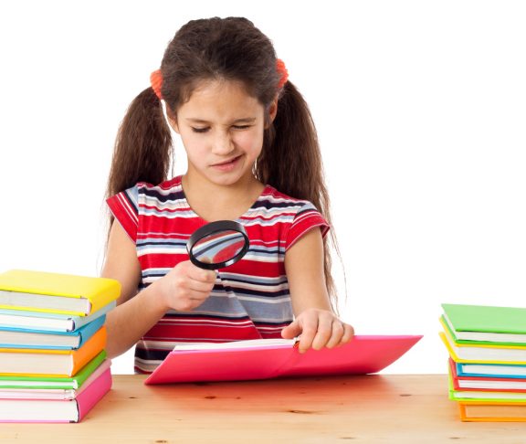 Girl reading the books on the desk with magnifying glass, isolated on white