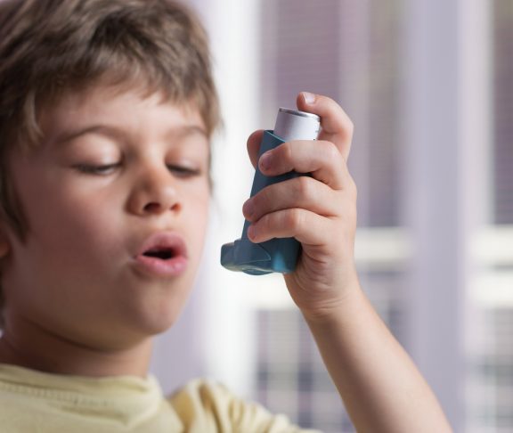 Boy using asthma inhaler to treat inflammatory disease, wheezing, coughing, chest tightness and shortness of breath. Allergy treating concept. Selective focus on inhaler.