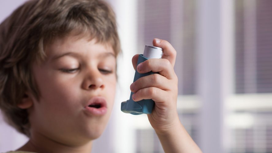 Boy using asthma inhaler to treat inflammatory disease, wheezing, coughing, chest tightness and shortness of breath. Allergy treating concept. Selective focus on inhaler.