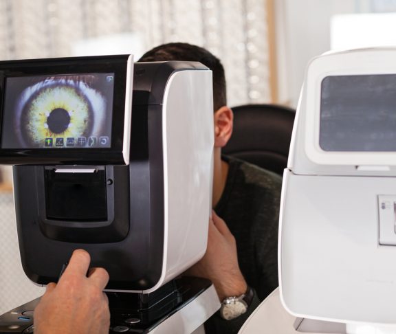 Ophthalmologist examining young man with optometric machine in optics store