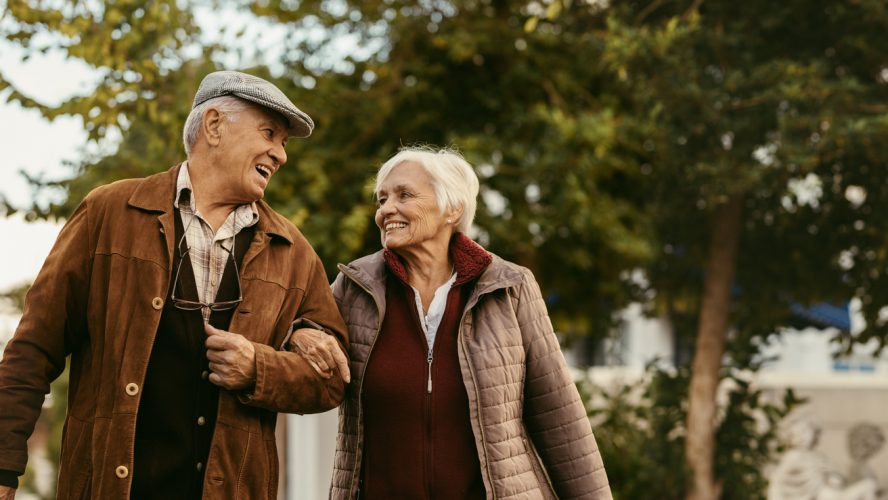 Portrait of happy retired man and woman in warm clothing walking outdoors on street. Loving senior couple enjoy a walk together on a winter day.