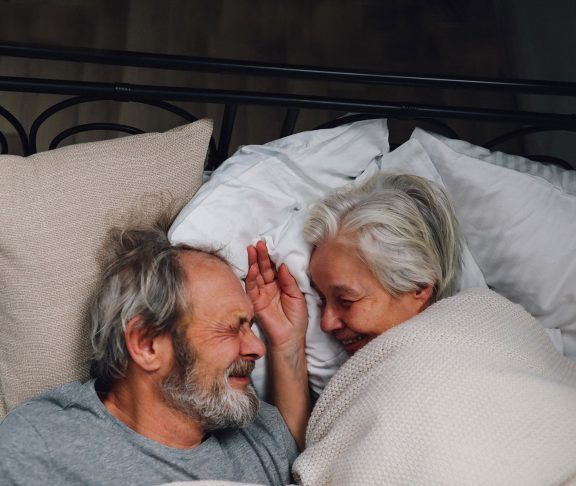 älteres Paar liegt zusammen im Bett und lächelt sich an