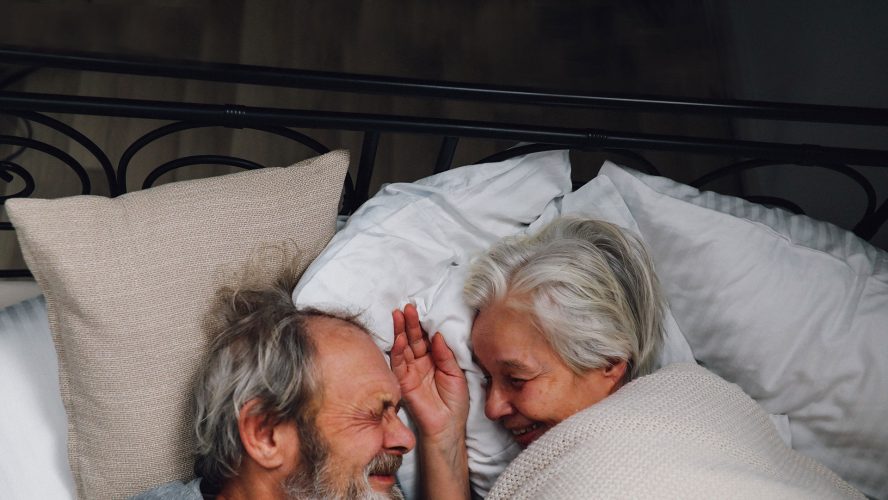 älteres Paar liegt zusammen im Bett und lächelt sich an