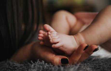 Hand der Mutter hält Füße ihres Neugeborenen Kindes