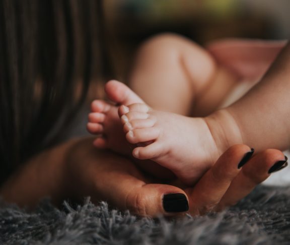 Hand der Mutter hält Füße ihres Neugeborenen Kindes