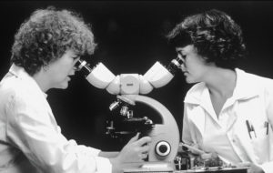 schwarz weiß bild, zwei Frauen schauen in ein Mikroskop rein