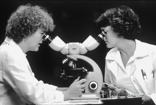 schwarz weiß bild, zwei Frauen schauen in ein Mikroskop rein
