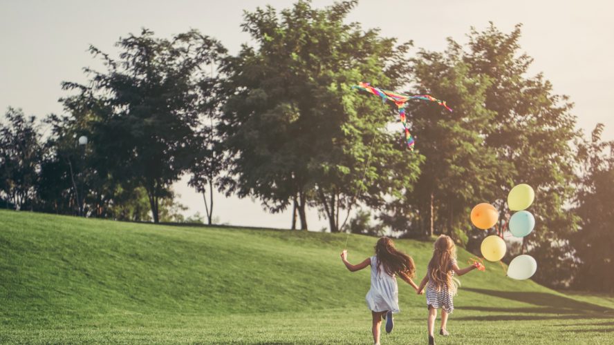 Little pretty girls having fun outdoor. Two cute girls are running on green grass with air balloons. Best friends