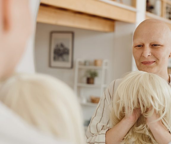 Syöpää sairastava nainen katsoo peiliin ja pitelee aidon näköistä peruukkia