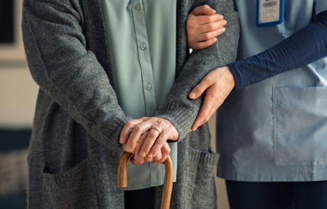 Close up hands of caregiver doctor helping old woman at private clinic. Close up of hands of nurse holding a senior patient with walking stick. Elder woman using walking cane at nursing home with nurse holding hand for support.