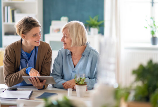 Caregiver or healthcare worker with senior woman patient, using tablet and explaining.