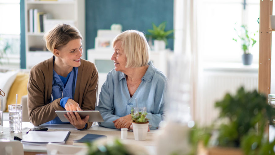 Caregiver or healthcare worker with senior woman patient, using tablet and explaining.
