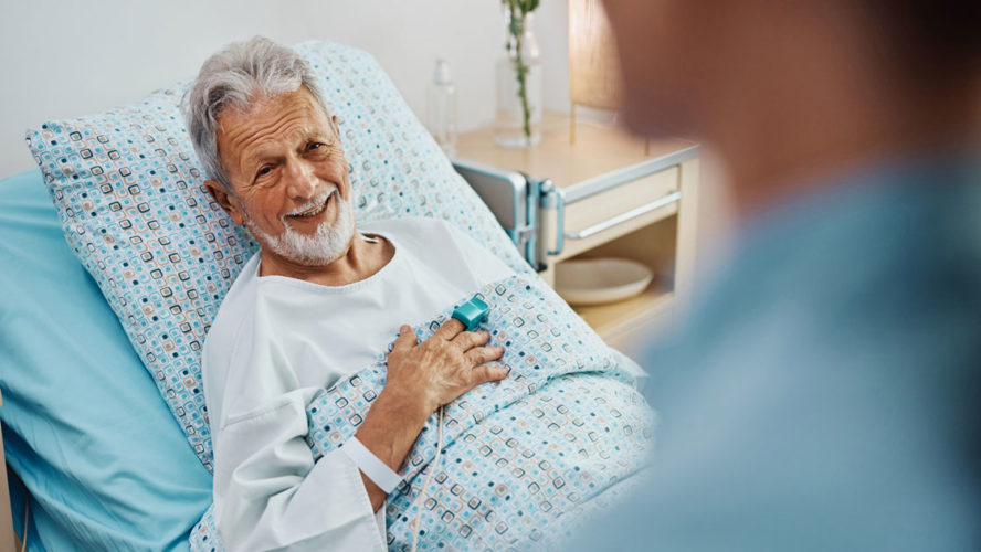 Happy senior patient talking to a nurse while recovering in the hospital ward.