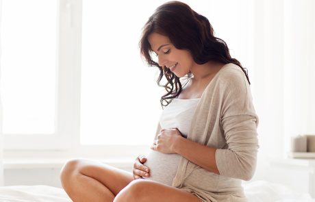 Vrouw met zwangere buik zit op bed