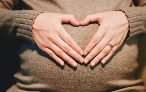 Zwangere vrouw legt handen op haar buik